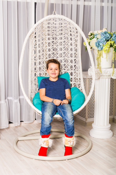 Портрет белого улыбающегося смеющегося мальчика, сидящего в кресле и смотрящего прямо в камеру
. - Фото, изображение