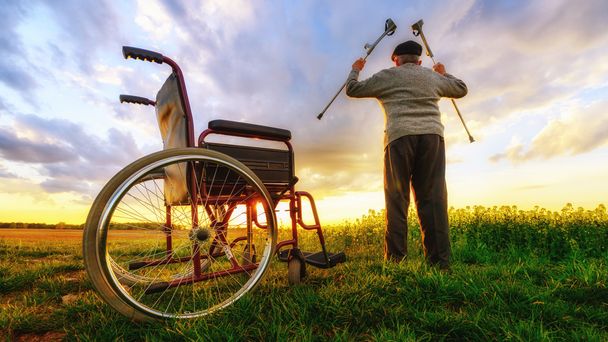 Θαύμα αποκατάστασης: παλιά ο άνθρωπος σηκώνεται από το αναπηρικό αμαξίδιο και θέτει τα χέρια πάνω  - Φωτογραφία, εικόνα
