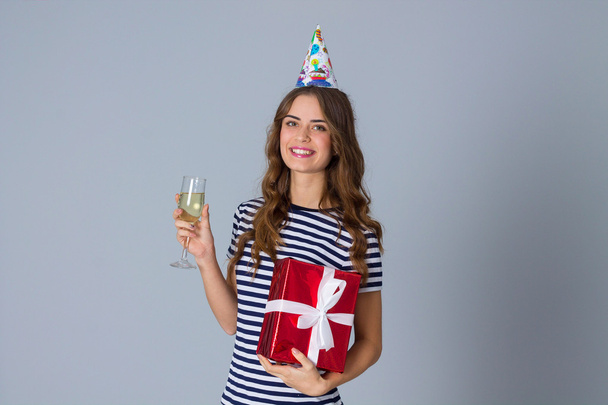 Mujer en gorra celebración sosteniendo un regalo y un vaso
 - Foto, imagen
