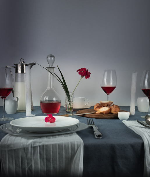 still life. jug of milk, rose wine in glasses, bun, white candles on a blue tablecloth - Photo, image