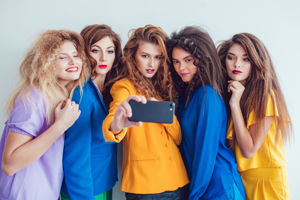Fashion girls in bright clothes make selfie. Beautiful women with professional makeup and crazy hair style, over white background. - Valokuva, kuva