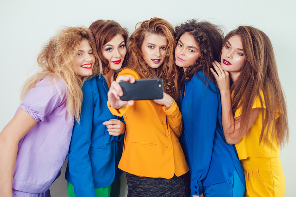 Mode meisjes in lichte kleren maken selfie. Mooie vrouwen met professionele make-up en gek kapsel, op witte achtergrond. - Foto, afbeelding