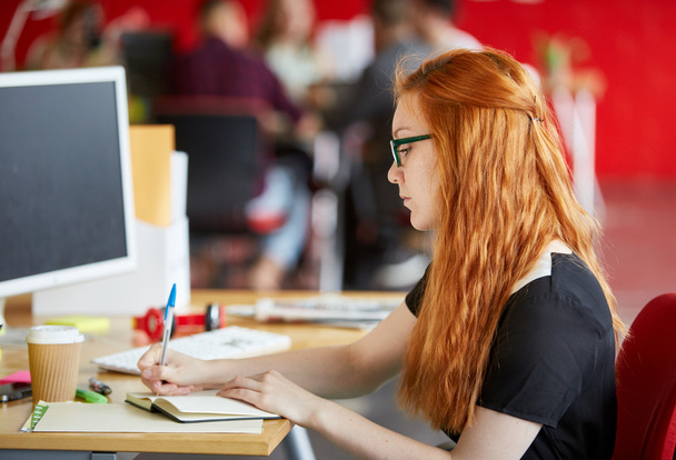 Designer feminina confiante trabalhando em sua mesa no espaço de escritório criativo vermelho
 - Foto, Imagem
