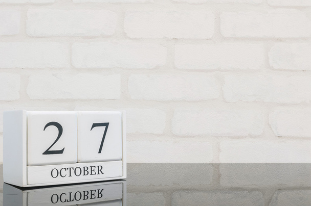 Gros plan calendrier en bois blanc avec mot noir 27 octobre sur table en verre noir et mur de briques blanches fond texturé avec espace de copie, mise au point sélective au calendrier
 - Photo, image