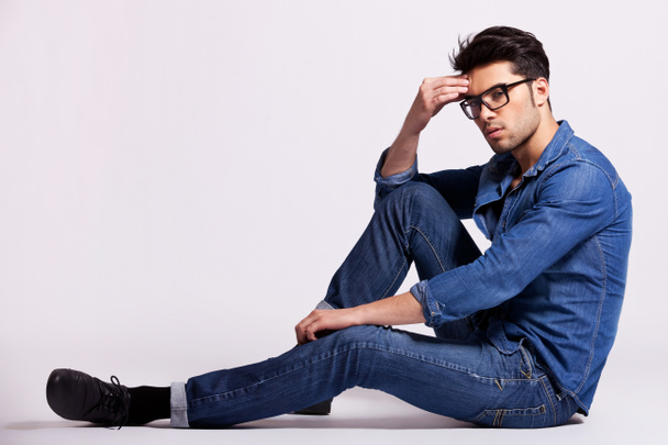 mannelijk model zittend op een grijze achtergrond en denken - Foto, afbeelding