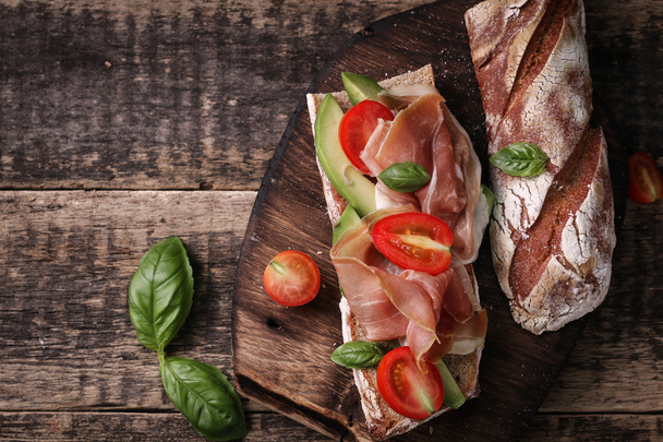 Ciabatta sandwich with prosciutto,avocado,cherry tomatoes and basil on dark background - Foto, immagini