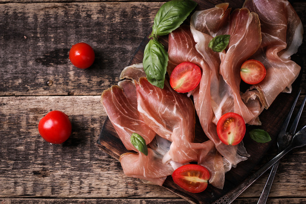 thin slices of prosciutto with mixed with basil, cherry tomatoes on wooden cutting board,vintage background - Foto, immagini