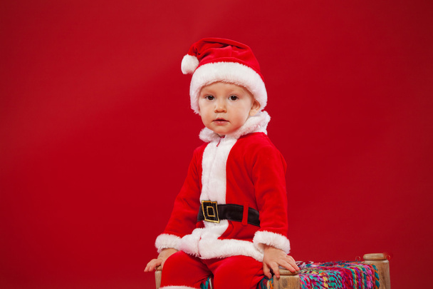 Beautiful little baby celebrates Christmas. New Years holidays red background - Photo, image