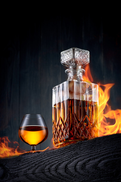Caraffa ardente e bicchiere di whisky su un tavolo di legno nero
 - Foto, immagini