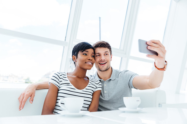 Smiling young couple making selfie photo on smartphone indoors - Foto, afbeelding
