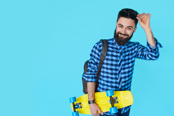 Hipster man over colorful blue background holding yellow skateboard - Foto, imagen