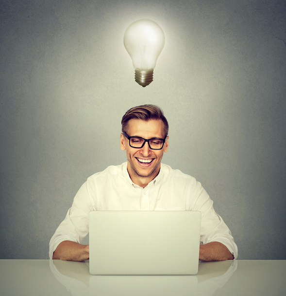 Hymyilevä mies tietokoneen edessä hehkulamppu pään päällä
 - Valokuva, kuva