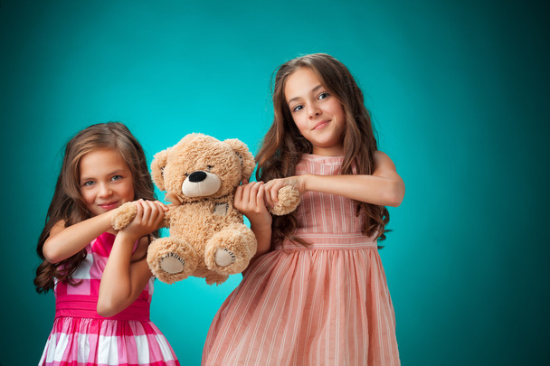 The two cute little girls on blue background with Teddy bear - Zdjęcie, obraz