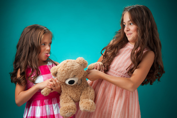 The two cute little girls on blue background with Teddy bear - Fotoğraf, Görsel
