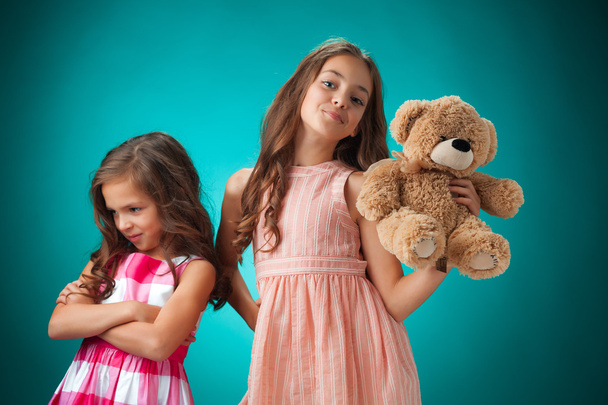 The two cute little girls on blue background with Teddy bear - Fotoğraf, Görsel