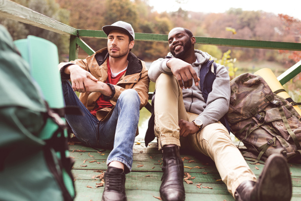 Young men with backpacks sitting on pier - Fotografie, Obrázek