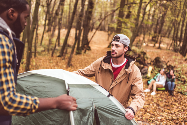 Men pitching tent in autumn forest  - 写真・画像