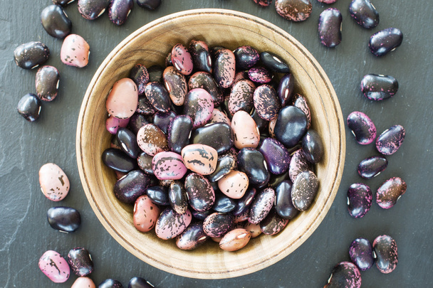 grain purple beans of different colors in a wooden bowl on a black background. vegetarian raw food. food color background - Fotó, kép