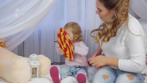 Little girl trying to eat painted lollipop near her mother - Felvétel, videó