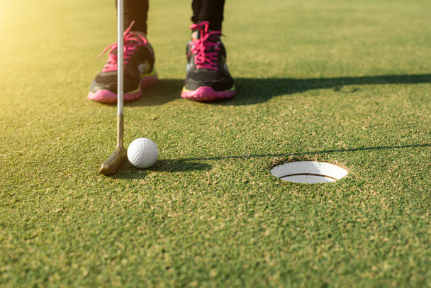 Игрок в гольф на зеленом поле кладет мяч для гольфа в лунку
.  - Фото, изображение