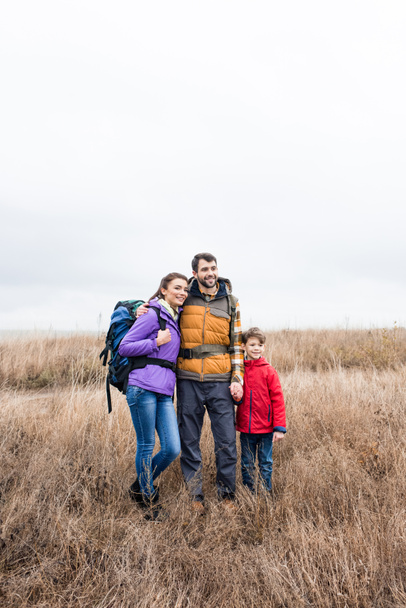 Happy family with backpacks standing in grass  - Photo, Image