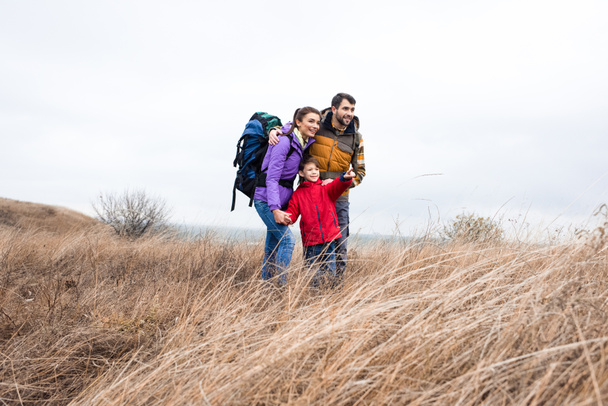 Happy family with backpacks standing in grass  - 写真・画像
