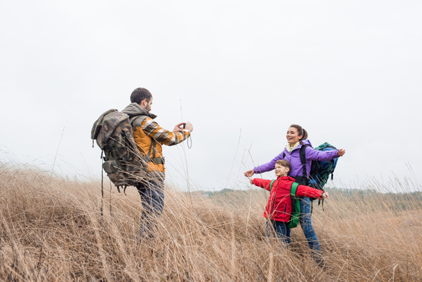 Hombre fotografiando esposa e hijo con mochilas
 - Foto, Imagen