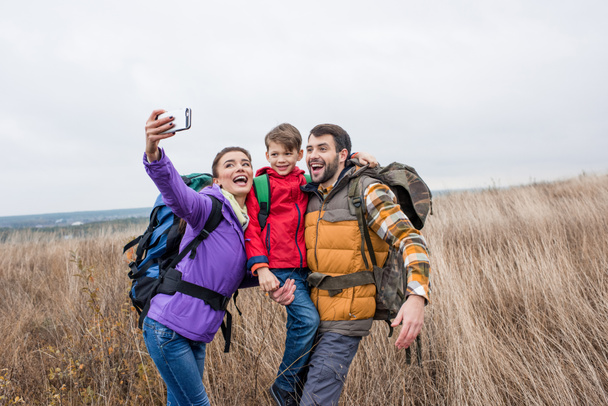 Onnellinen perhe reppuineen ottaa selfie
 - Valokuva, kuva