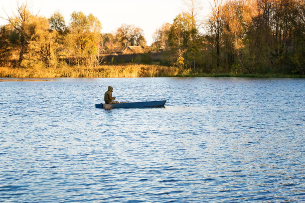 Autumn landscape: the lake and the fisherman on the boat. - Zdjęcie, obraz