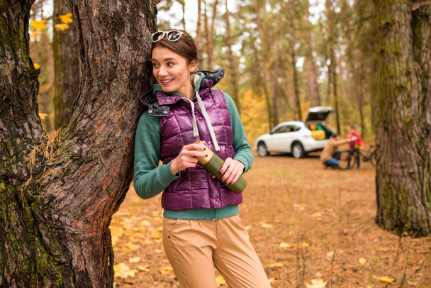 Smiling woman with thermos in autumn forest  - Foto, imagen