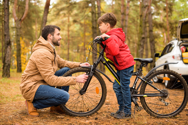 Isä opettaa poikaa ajamaan polkupyörällä
 - Valokuva, kuva