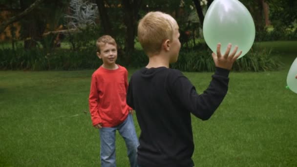 Three happy young children play a game in a park with balloons - slowmo handheld - Metraje, vídeo