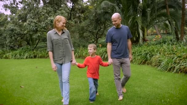 Vanhemmat pitävät poikaansa kädestä ja kääntävät hänet ylösalaisin kävellessään puistossa.
 - Materiaali, video