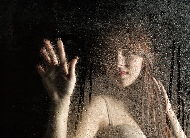 Smooth portrait of sexy model, posing behind transparent glass covered by water drops. - Foto, immagini