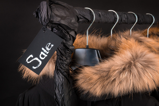 lot of black coats, jacket with fur on hood hanging  clothes rack.  background. Sale inscription.  friday.Close up. - Fotografie, Obrázek