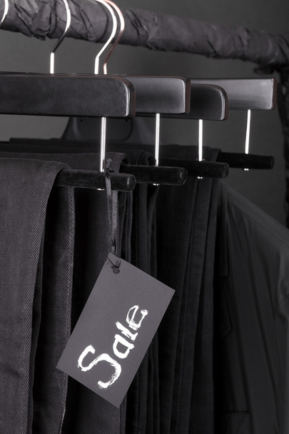 lot of black pants jeans and jacket hanging on clothes rack.  background. sale sign.  friday. Close up. - Fotografie, Obrázek