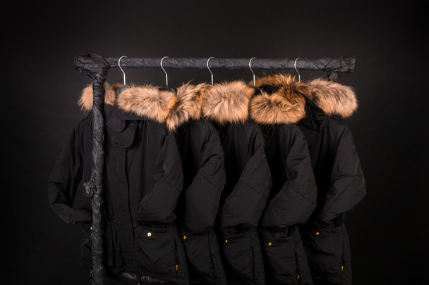 lot of black coats, jacket with fur on hood hanging  clothes rack.  background. - Fotografie, Obrázek