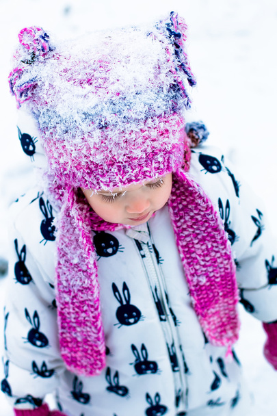 Criança em dia nevado. Retrato de menina em terno de neve branca e chapéu rosa no parque de inverno. em
 . - Foto, Imagem