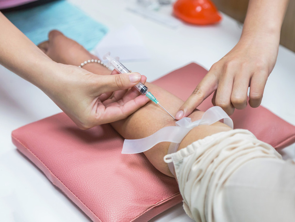 Acercamiento de la jeringa de la aguja de pinchazo enfermera en el paciente del brazo extracción de muestra de sangre
 - Foto, Imagen