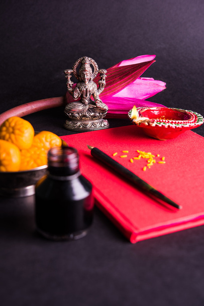 An auspicious Indian writing Shubha Labh means 'Goodness' & 'Wealth', over Red accounting note book / 'bahi khata' with goddess Laxmi, diya, sweets and lotus and pen with ink on laxmi pujan, on diwali - Photo, Image