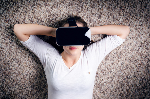 Woman with virtual reality goggles lie on a carpet. Studio. Woman show a gesture.  - Foto, afbeelding