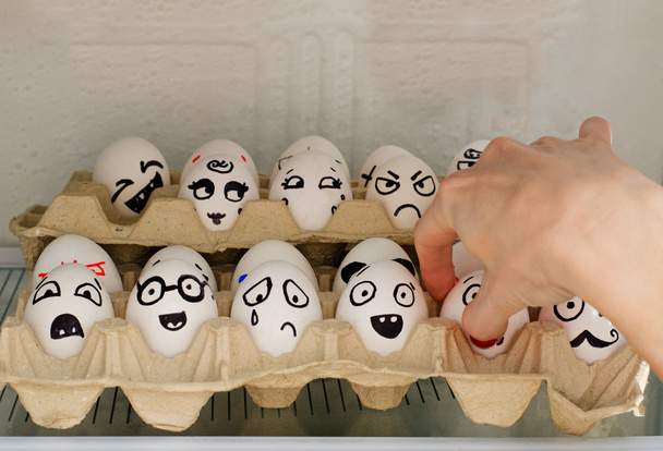Huevos con emociones pintadas en el refrigerador, una mano femenina toma uno de ellos
 - Foto, Imagen