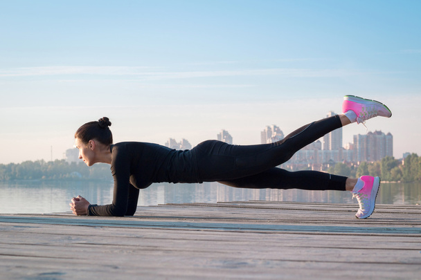 Pretty fitness woman exercises on pier during sport training - Photo, Image