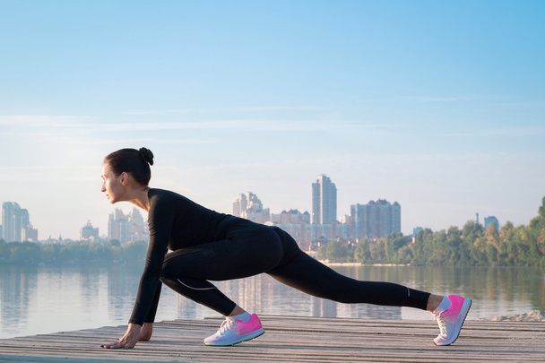 Young fitness woman exercises on pier during morning sport workout - Photo, Image