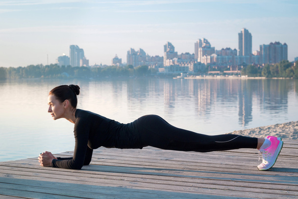Pretty fitness woman exercises on pier during morning sport training - Fotografie, Obrázek