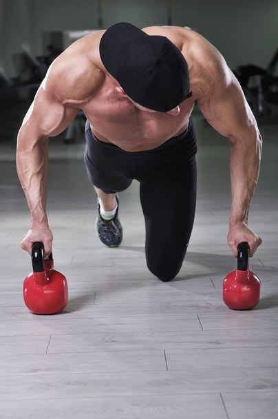Handsome powerful athletic man performing push ups with kettle bell. Strong bodybuilder with perfect shoulders, biceps and triceps. - Foto, afbeelding