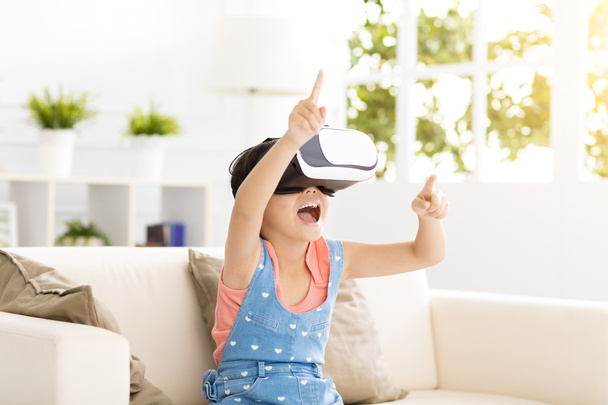 happy little girl with virtual reality headset sitting on sofa - Fotoğraf, Görsel
