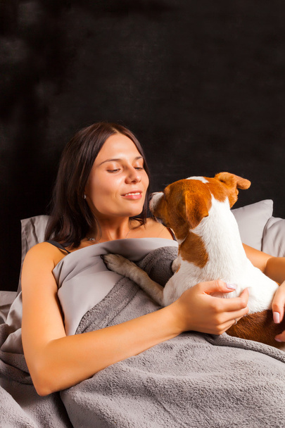 Young beautiful brunette woman plays in bed with her dog - Fotoğraf, Görsel