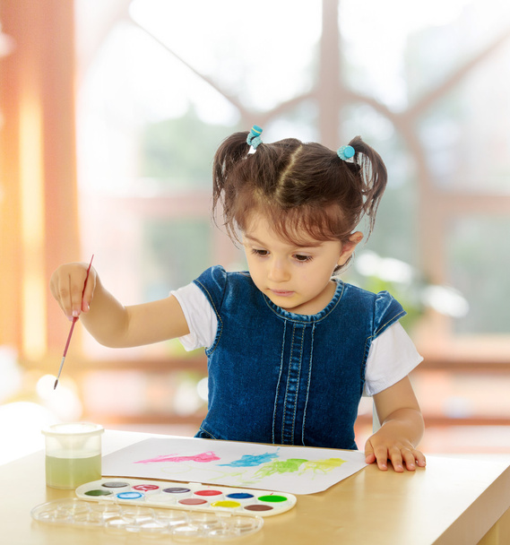 Little girl paints with watercolors at the table. - Fotó, kép