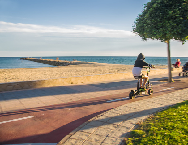 Genç adam sürme elektrikli scooter sonbahar Plajı. - Fotoğraf, Görsel